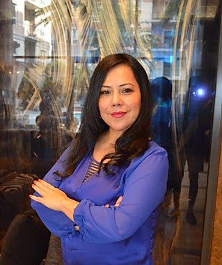 A woman in a blue blouse posing with crossed arms indoors.