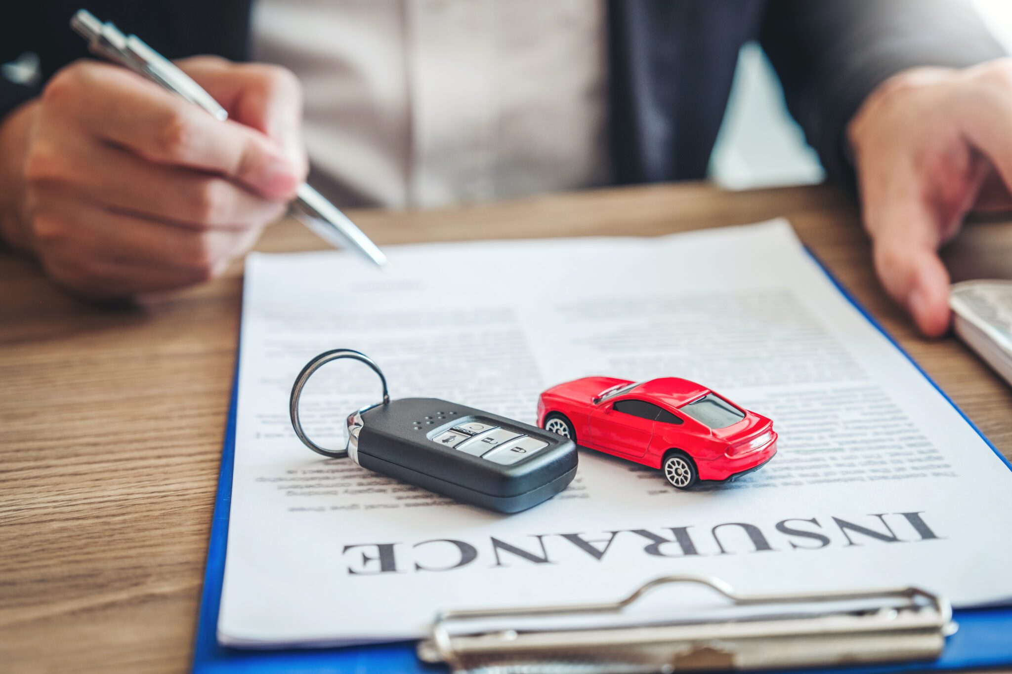 A person reviewing car insurance documents with a toy car and keys.