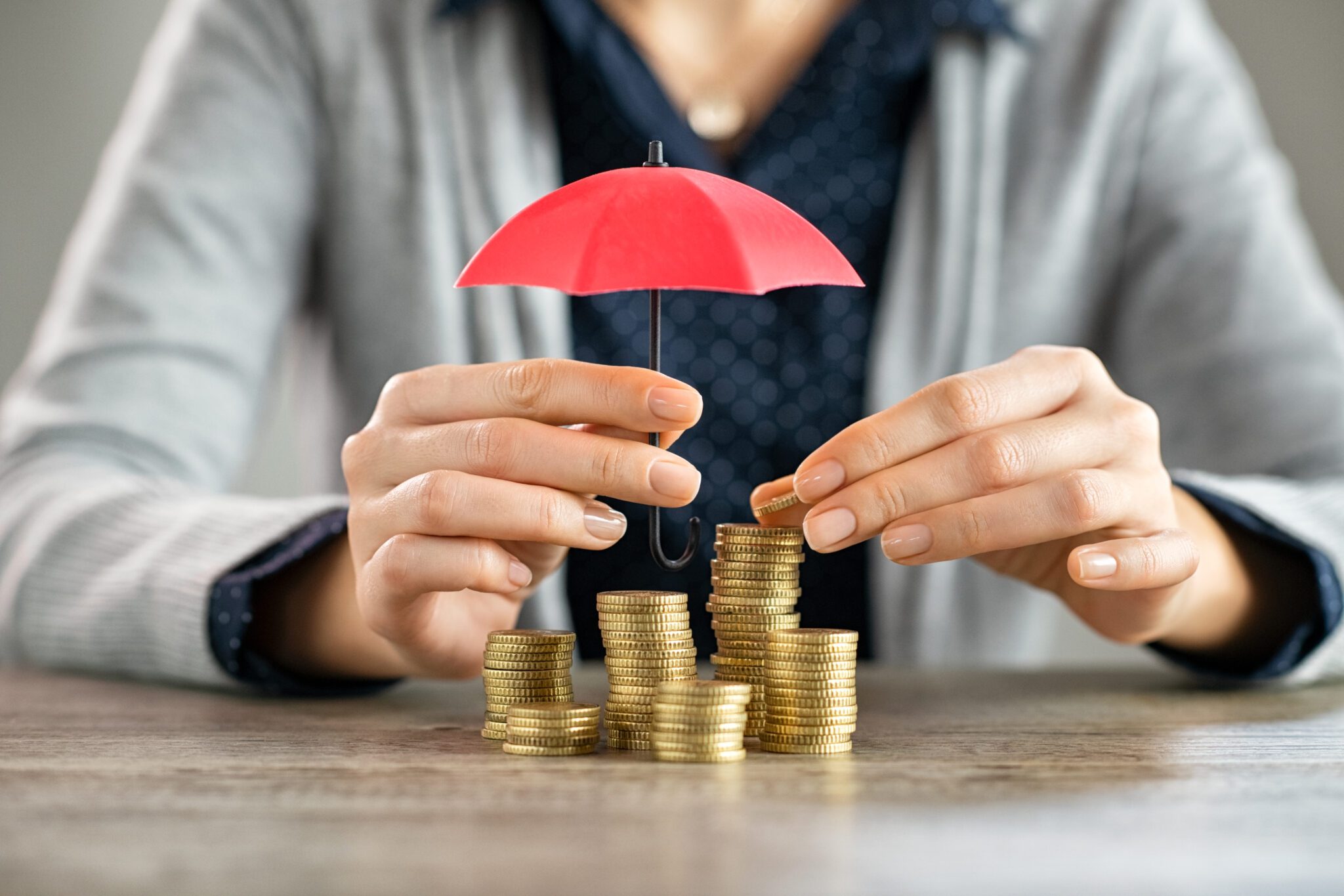 Person protecting stacked coins with a small red umbrella.