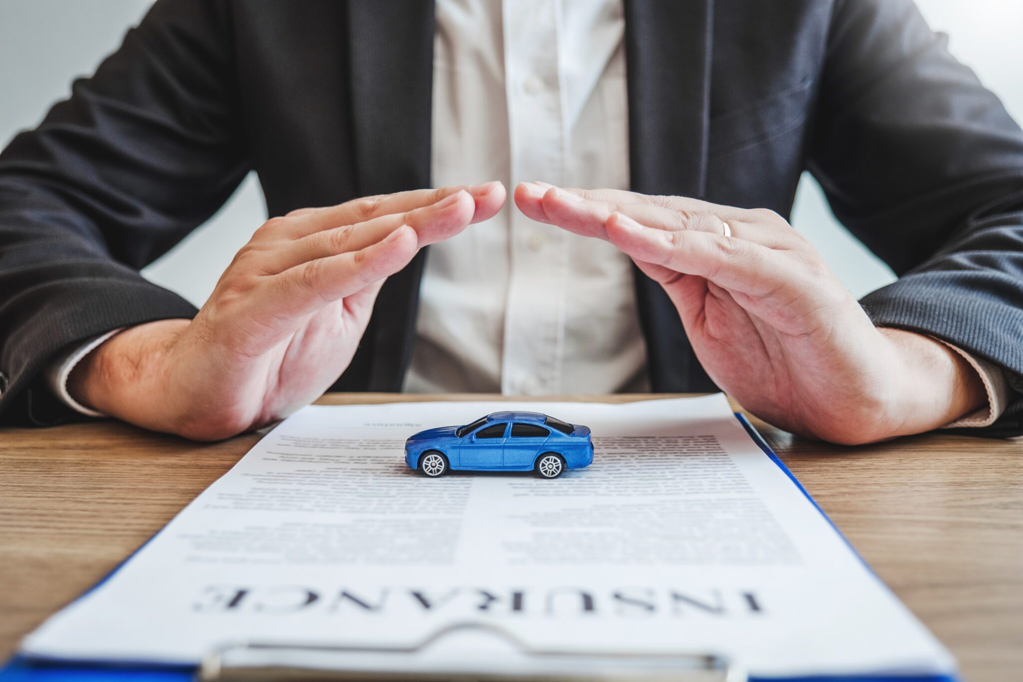 Businessman protecting a toy car over an insurance document.