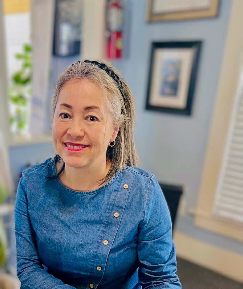 Smiling woman in a blue top with a cozy indoor background.